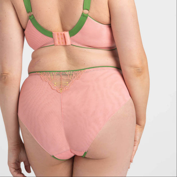 Woman wearing a pink lingerie set with green straps on a white background